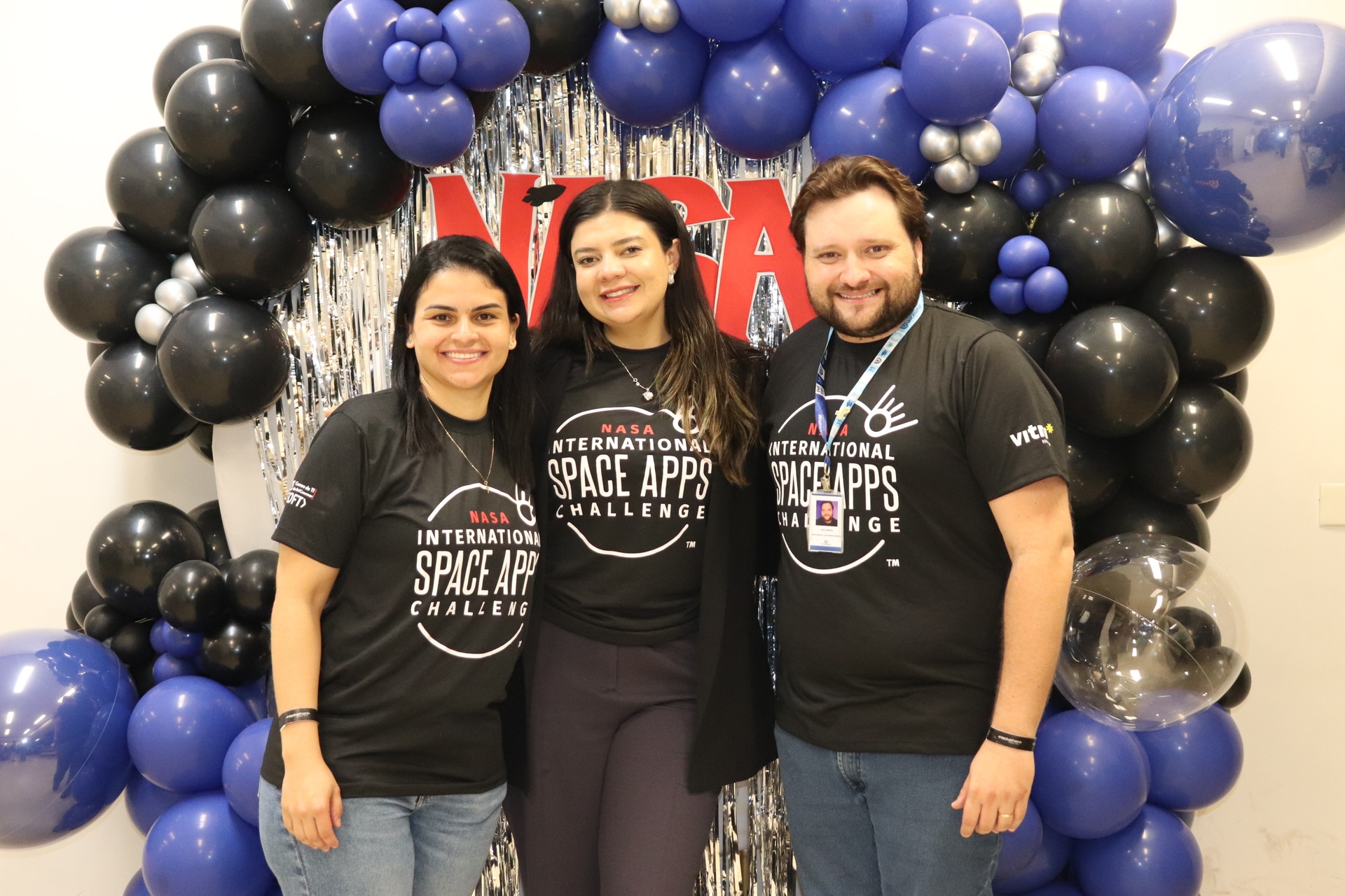 Duas representantes da Elotech, patrocinadora do hackathon, ao lado do professor João Ferlini durante o NASA Space Apps Challenge 2025 na UniCesumar.